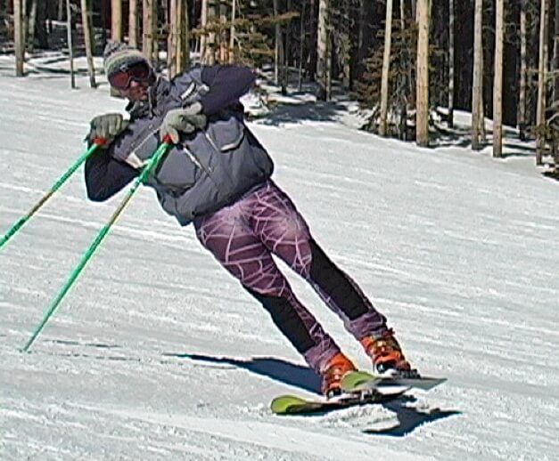 Skier ständig on snow with both legs long. Skier is leaning uphill using poles to balance.